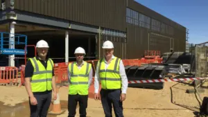 Three men in construction gear standing in front of a building site under development.