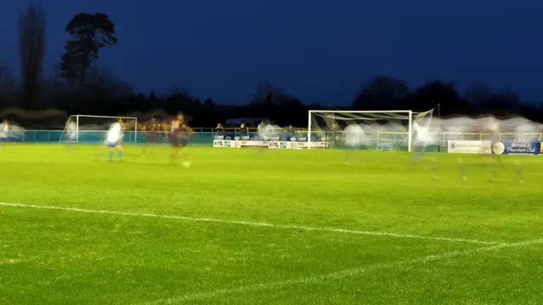 Evening football match taking place on a local grass pitch in the UK.