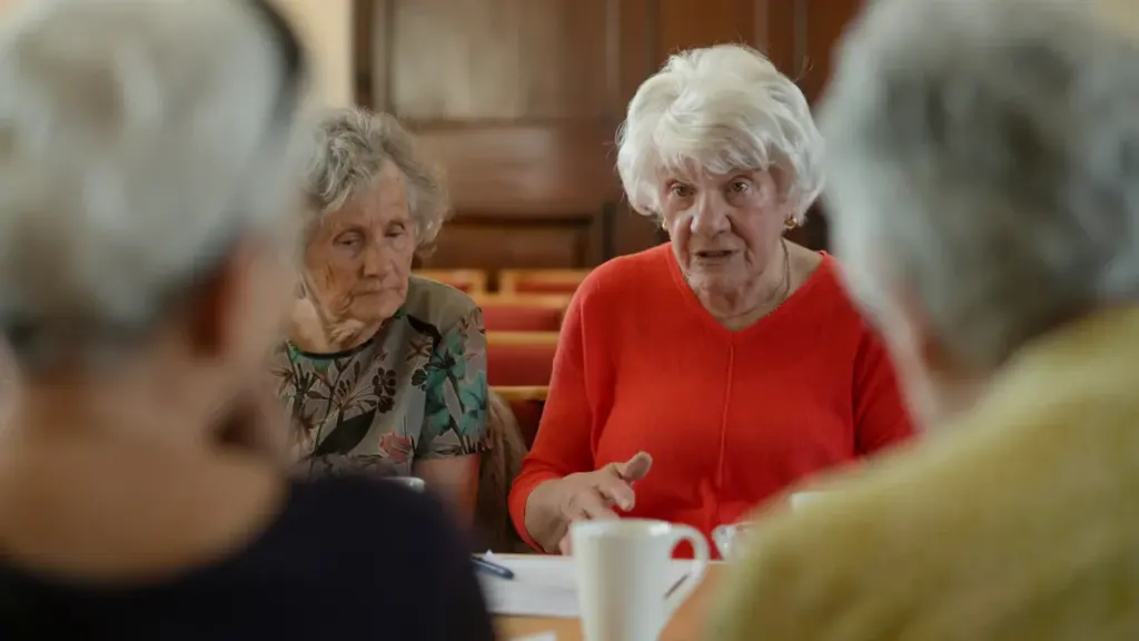 Group of elderly people engaged in a serious discussion around a table.