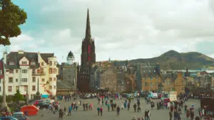 Crowded Royal Mile square in Edinburgh with historic stone buildings during a bright afternoon.