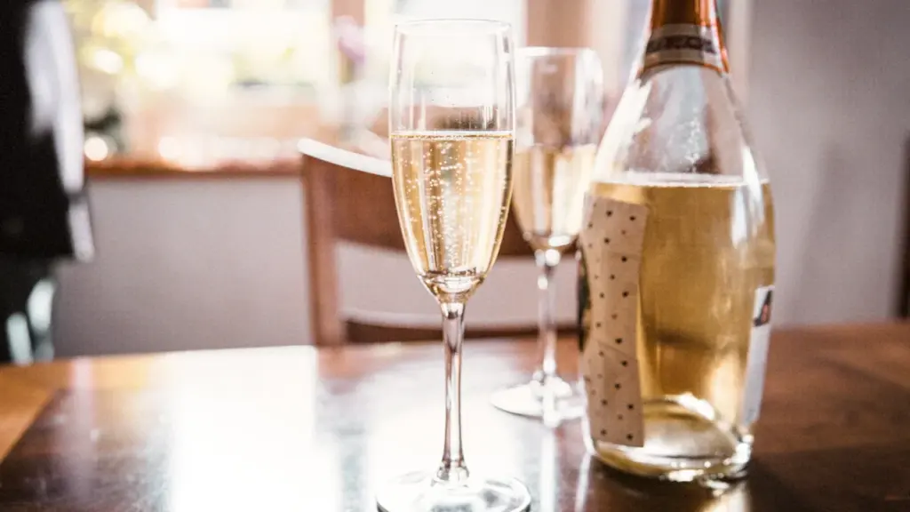A clear glass of sparkling Prosecco beside a bottle on a wooden table.