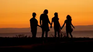 Silhouette of a family holding hands against a warm golden sunset background.