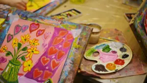 Close-up of vibrant children's paintings and art supplies on a wooden table.