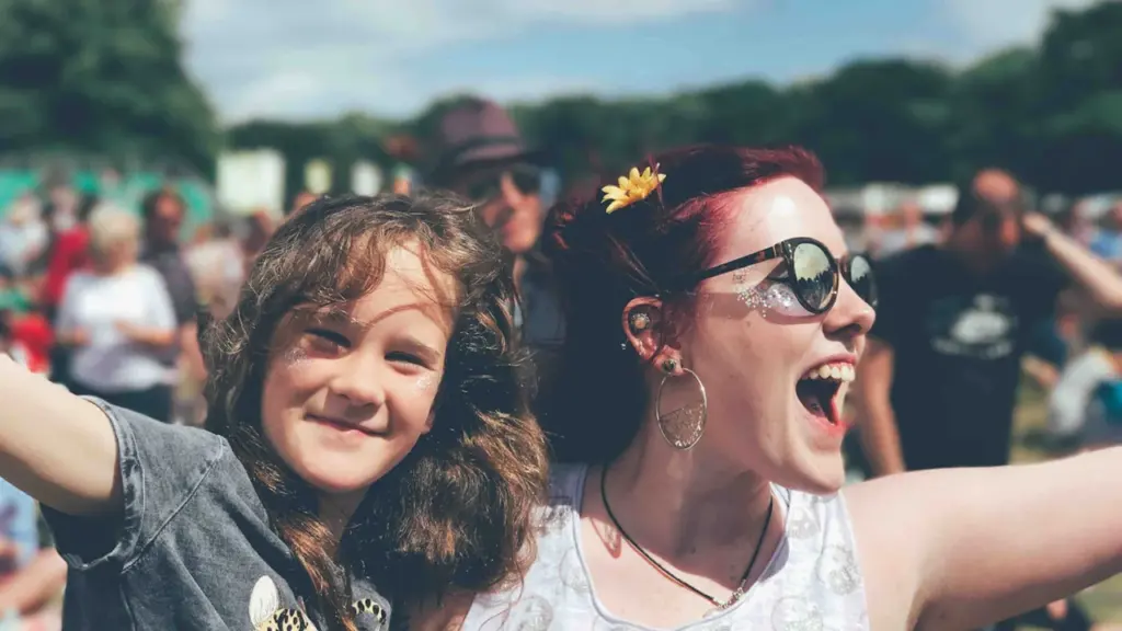 A woman and young girl enjoying music at a sunny outdoor festival in England.