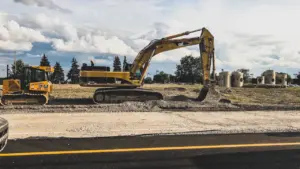 Large yellow construction excavators parked on a gravel site next to a roadway.