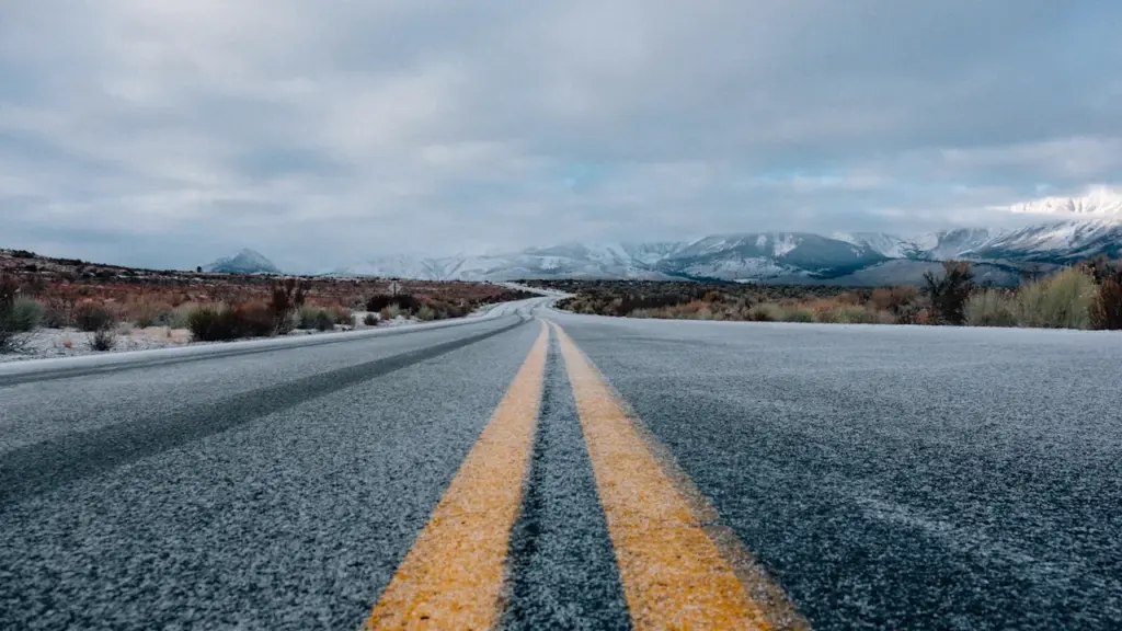 An empty asphalt road stretching toward snow-capped mountains under a cloudy sky.