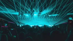 Vibrant teal laser lights illuminate a crowd at an energetic nightclub event.