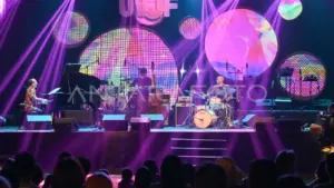 Live band performance under bright purple lights with abstract background screens on stage