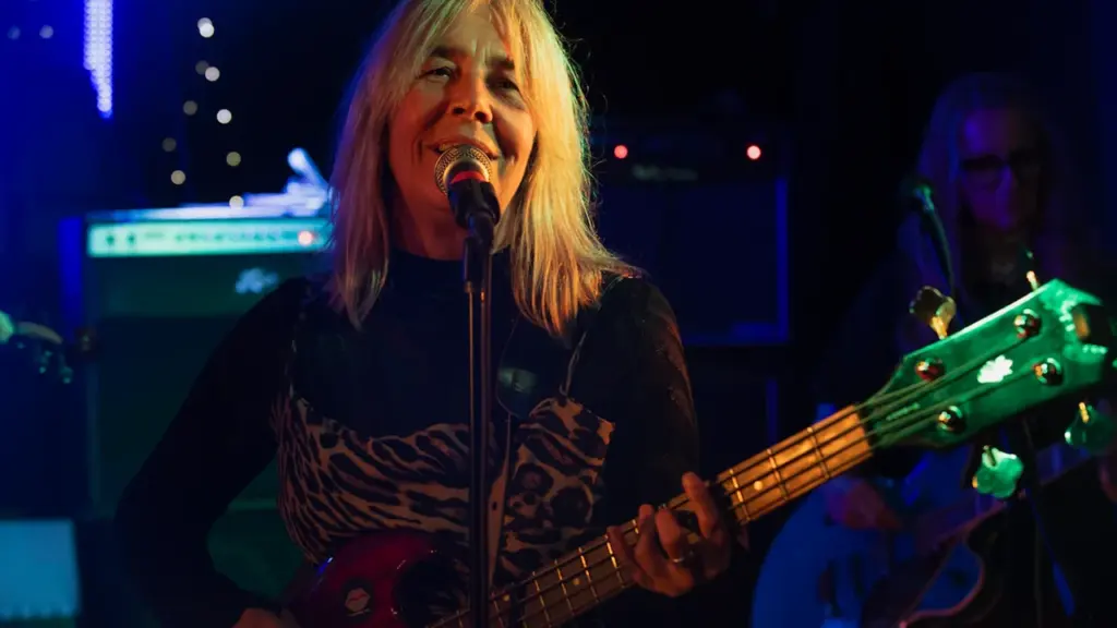 Female musician playing bass guitar and singing on stage at a live concert.