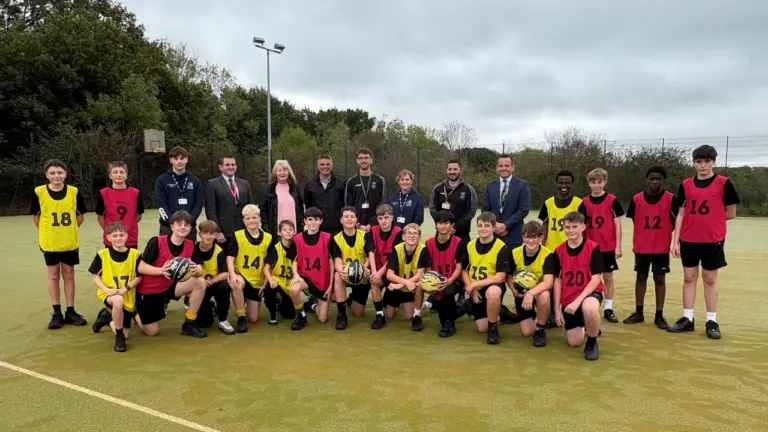 A large group of teenage boys and adult staff posing on an outdoor sports field.