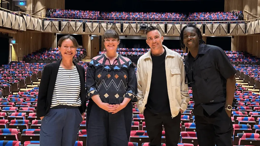 Four people stand in front of rows of empty patterned theater seats inside auditorium.