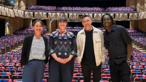 Four people stand in front of rows of empty patterned theater seats inside auditorium.